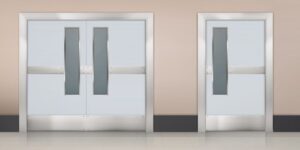 Two closed hospital doors with metal frames and vertical glass panels, set in a beige wall with a tiled floor, exemplify the reliability of a commercial fire rated door from Singapore’s trusted provider, Boon Woh.